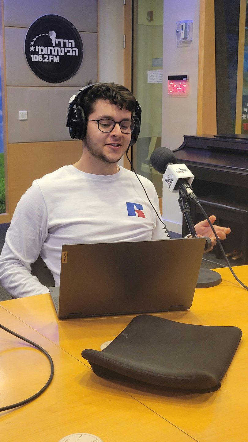 Mężczyzna w okularach i słuchawkach mówi do mikrofonu studyjnego.
